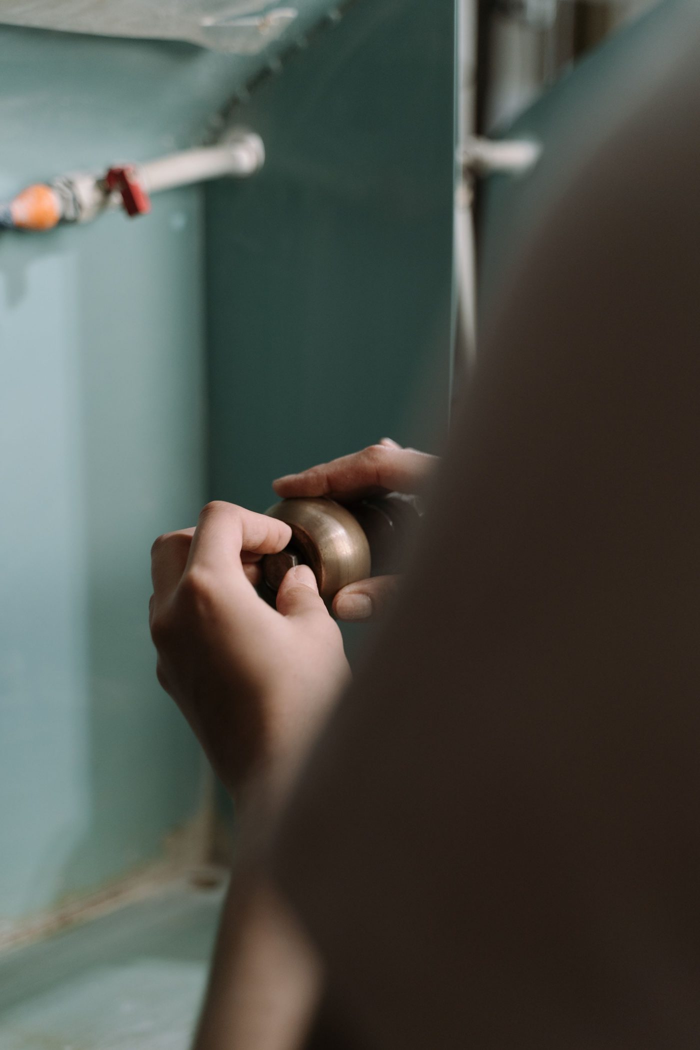 Hands turning a fitting on the pipework under a kitchen sink in low light