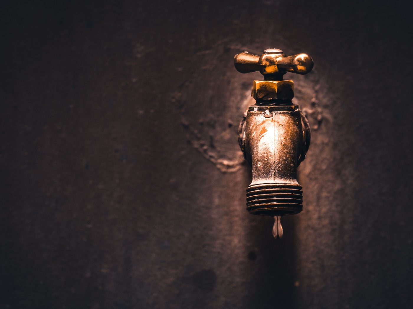 Old brass tap with a single drip against a dark wall