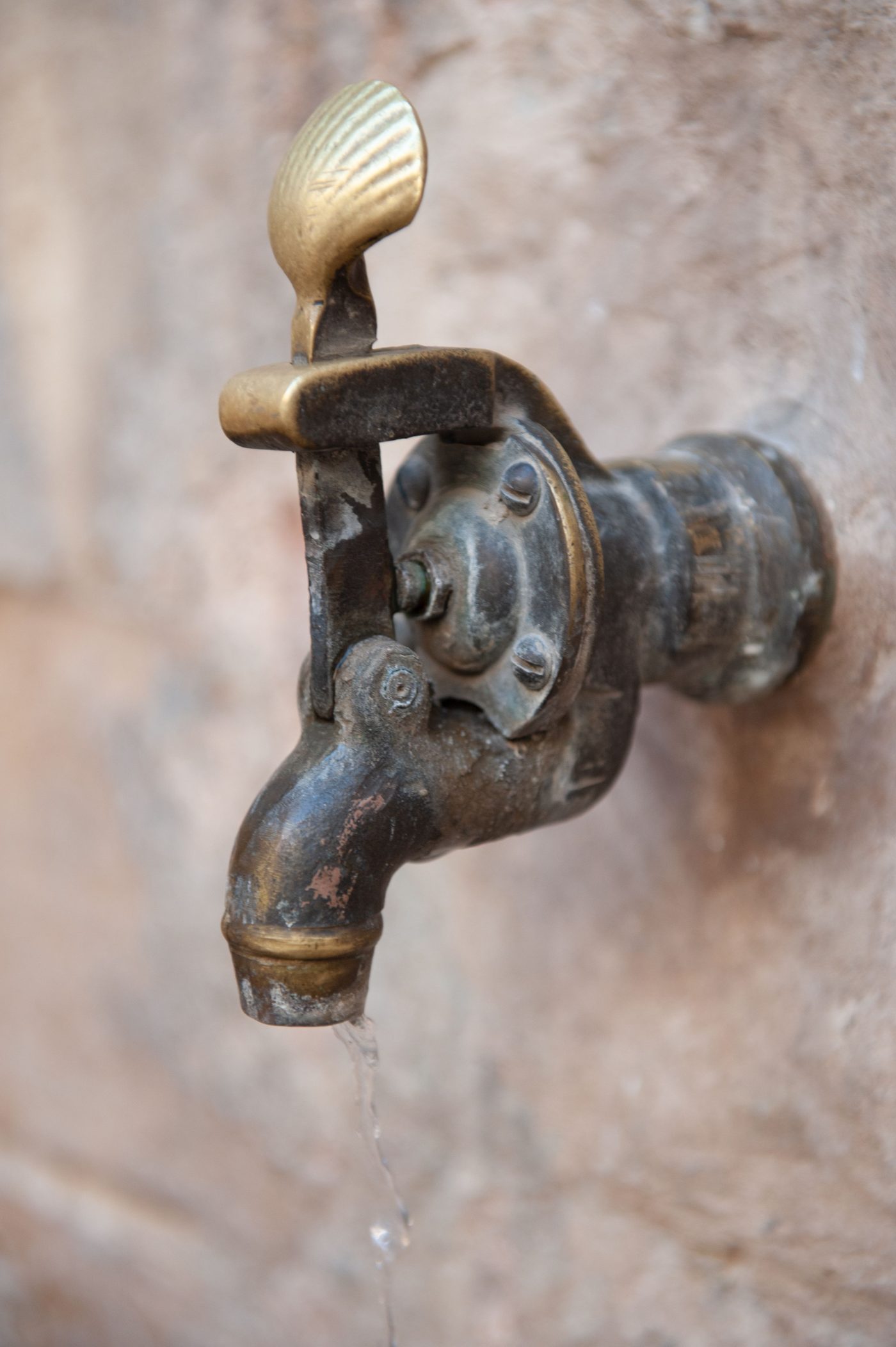 Old brass tap and valve body on a wall with a drip of water